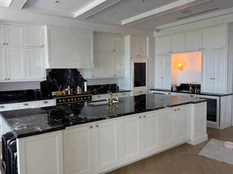 A finished kitchen with a black stone island and backsplash, veined in white.